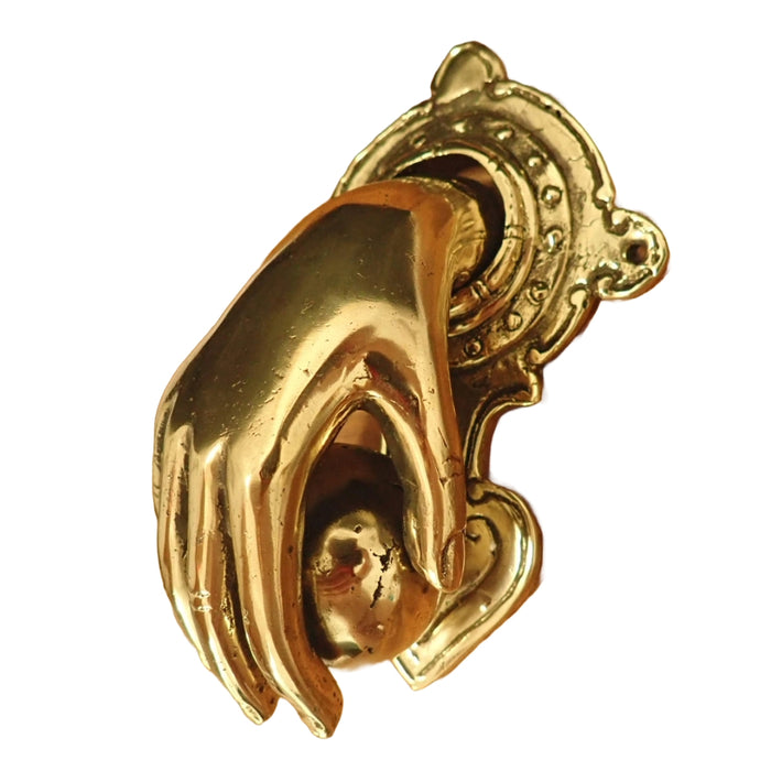 A highly polished brass door knocker shaped like a hand holding a ball