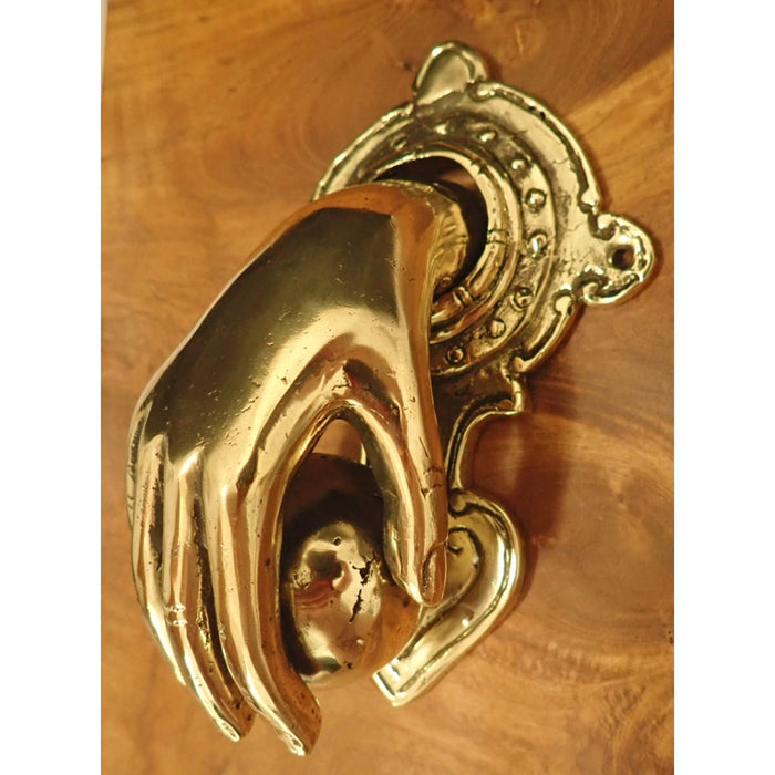 A highly polished brass door knocker shaped like a hand holding a ball