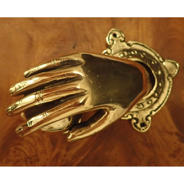 A highly polished brass door knocker shaped like a hand holding a ball