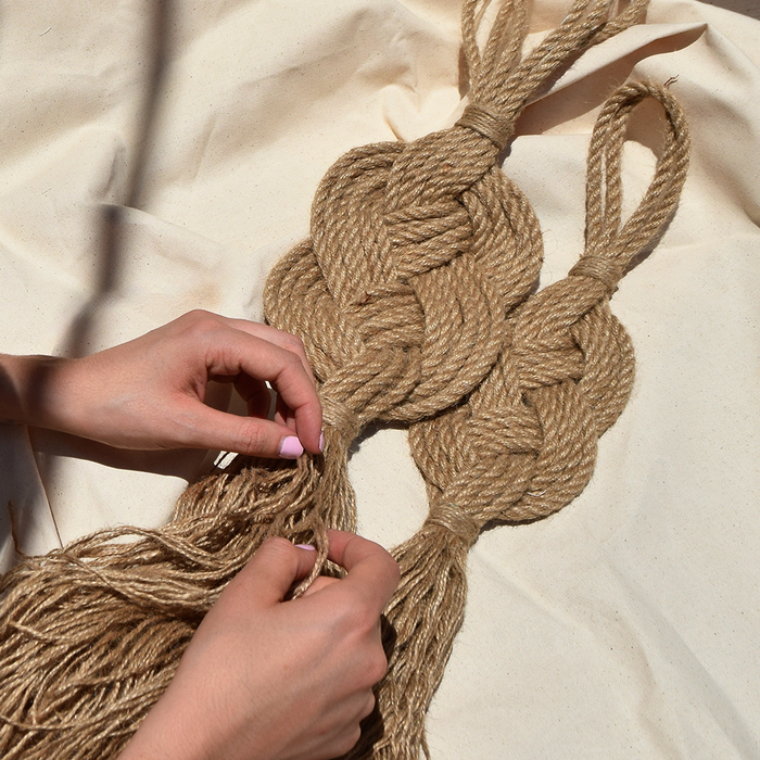 A handmade wall hanging decoration made with natural jute fiber rope, featuring a braided geometric pattern.