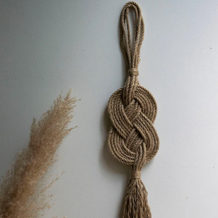 A handmade wall hanging decoration made with natural jute fiber rope, featuring a braided geometric pattern.