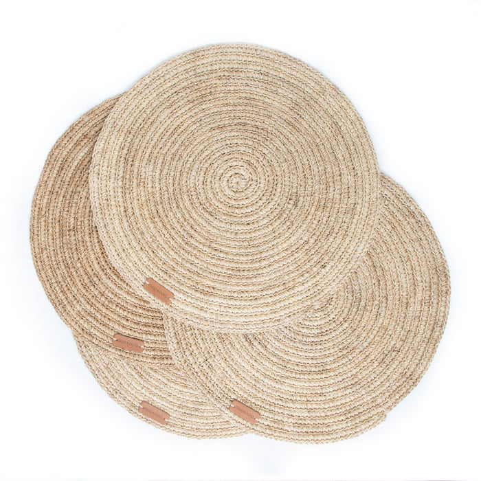 Stack of four round handwoven, natural fibre placemats made by Colombian artisans in beige tones.