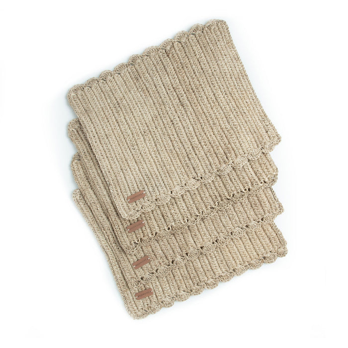 A stack of four rectangular, beige, handwoven placemats with a simple pattern.