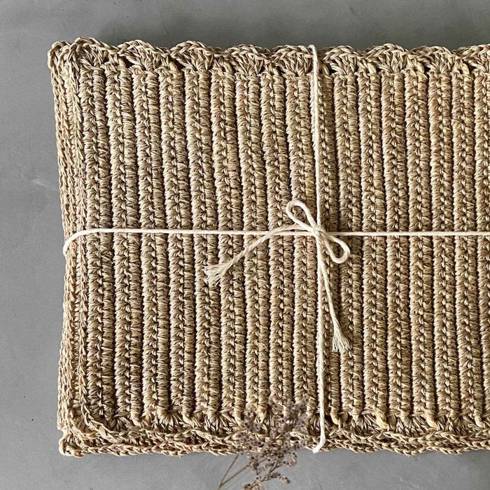 A rectangular, beige, handwoven placemat with a simple pattern, tied up with a natural fibre twine.